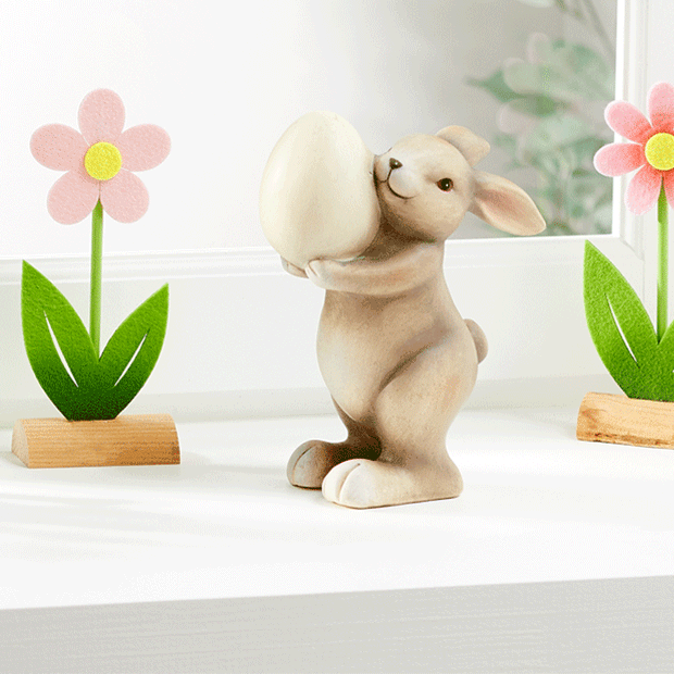 Keramik-Hase mit Ei vor bunten Blumen-Deko – Osterdekoration. Großhandel für Deko- & Geschenkartikel