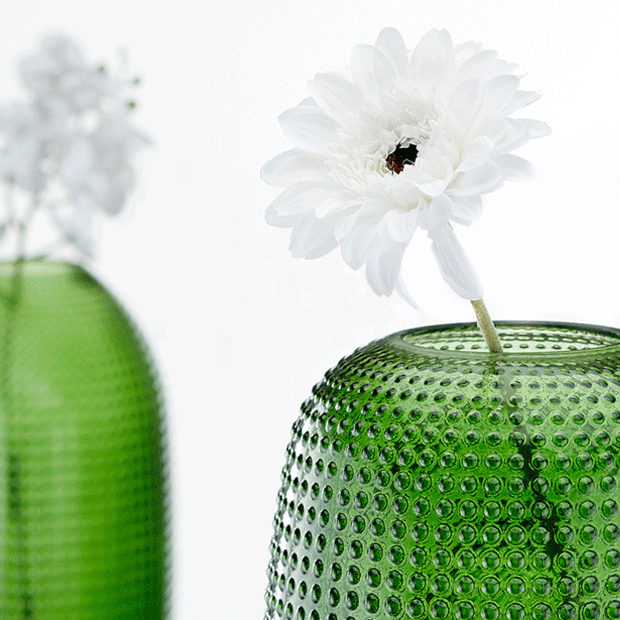 Grüne Glasvase mit weißer Kunstblume – moderne Wohnaccessoires. Großhandel für Deko- & Geschenkartikel